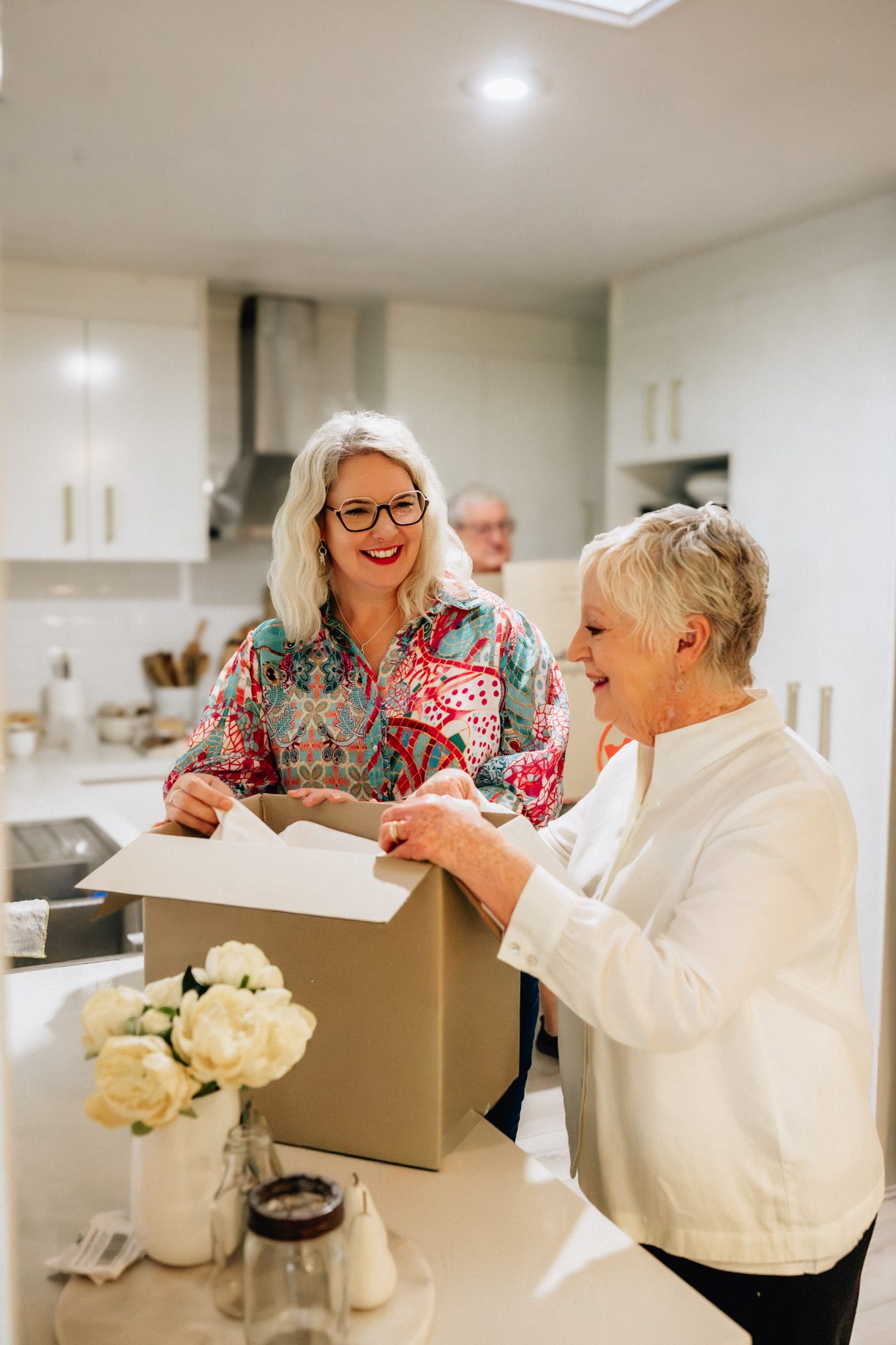 A woman and her client smiling together as they unpack a box in a bright kitchen